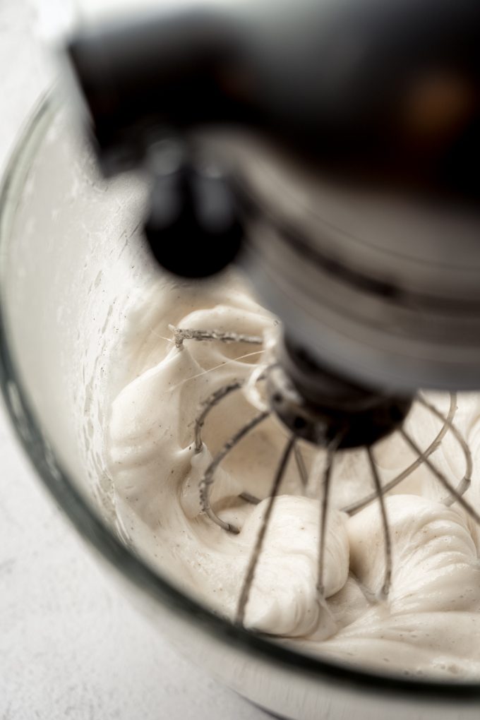 A mixer with homemade marshmallow mixture in the bowl with the whisk attachment.