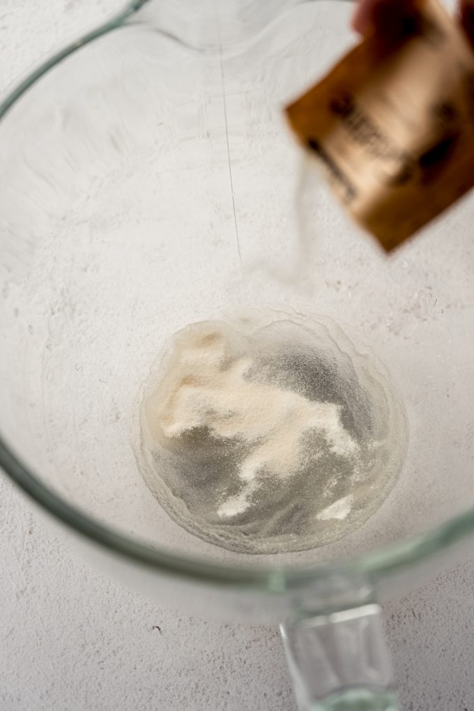 Someone is sprinkling a packet of gelatin over water in the bottom of a large glass bowl.