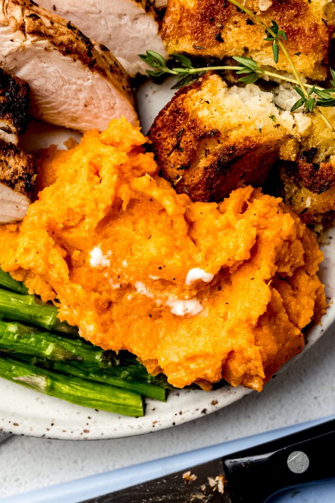 Mashed sweet potatoes on a plate with asparagus, stuffing, and turkey in the background.