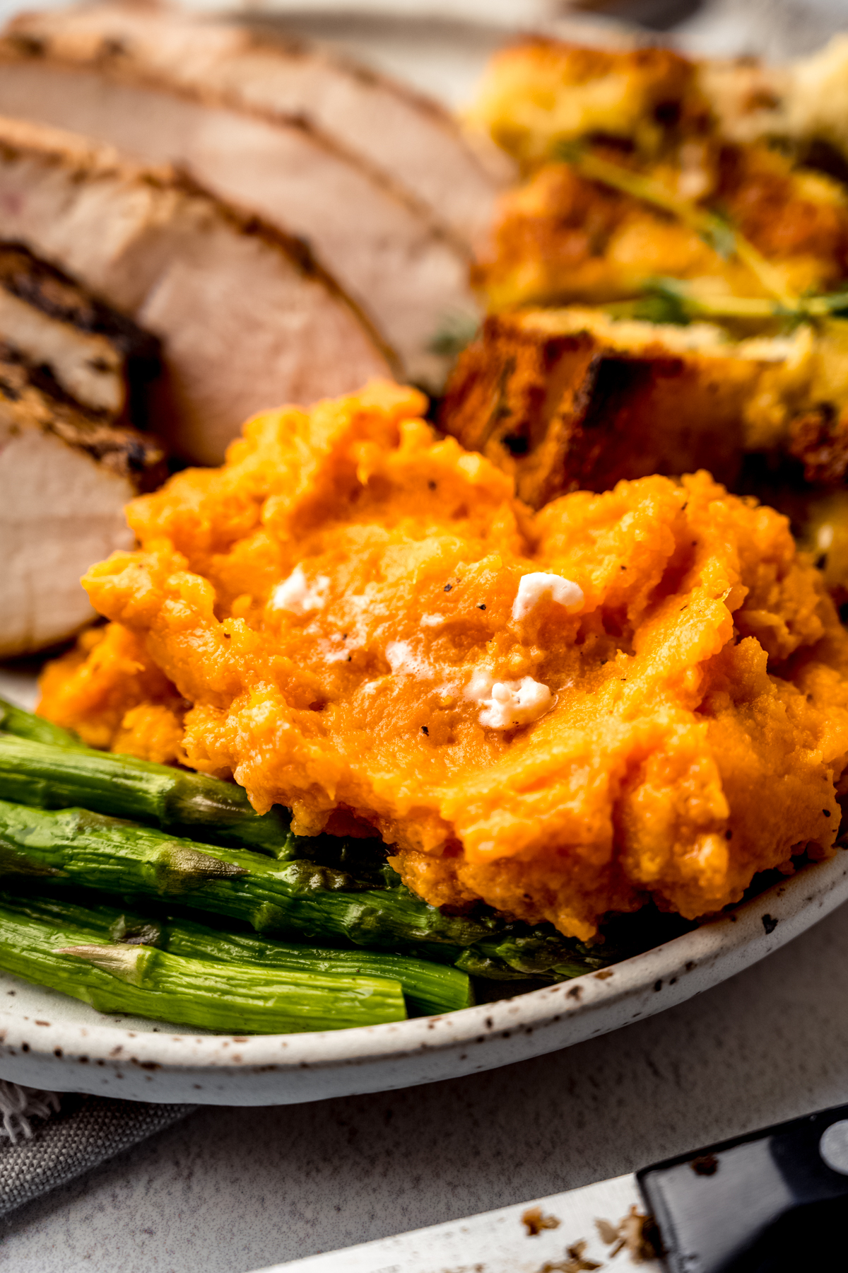 Mashed sweet potatoes on a plate with asparagus, stuffing, and turkey in the background.