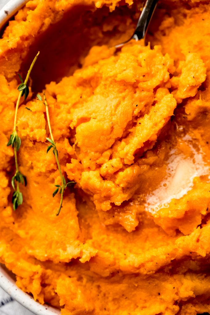 A closeup photo of mashed sweet potatoes in a bowl with a spoon.