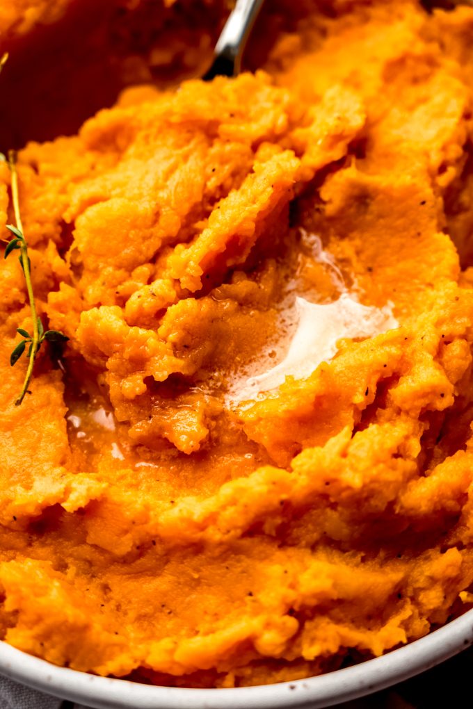 A closeup photo of mashed sweet potatoes in a bowl with a spoon.
