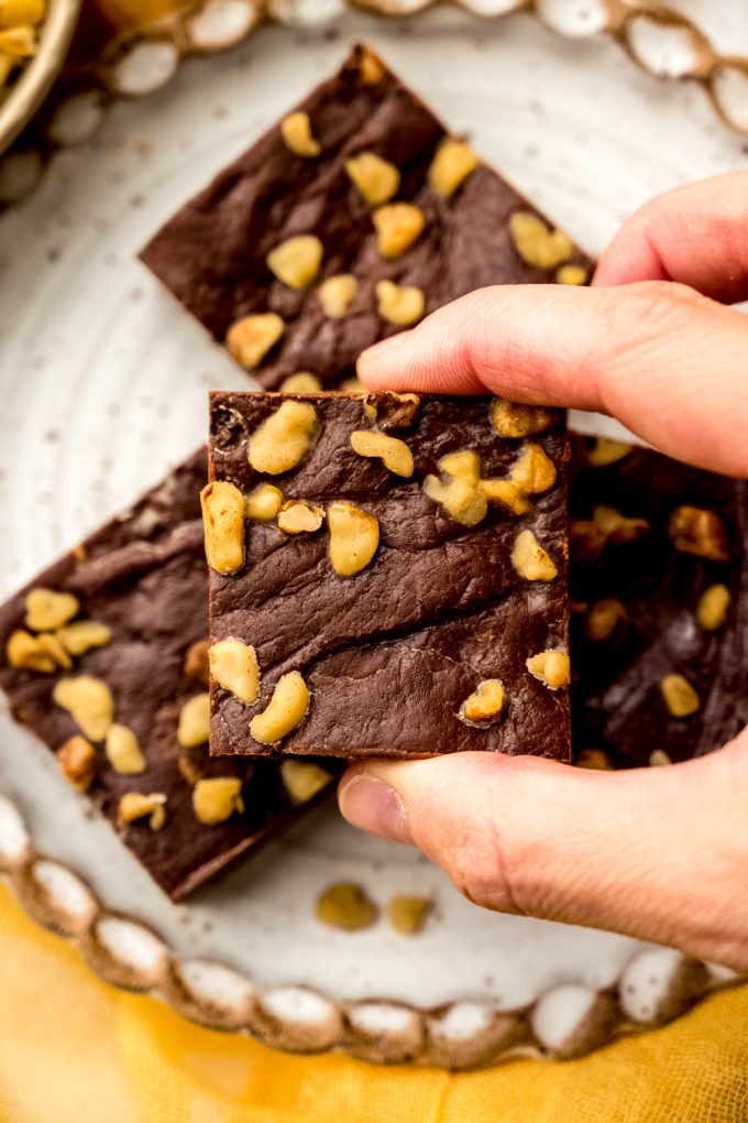 Someone is holding a piece of microwave fudge over a plate of other pieces of fudge.