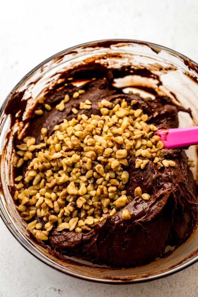 The base for microwave fudge in a bowl with walnuts and a spatula getting ready to someone to stir them in.