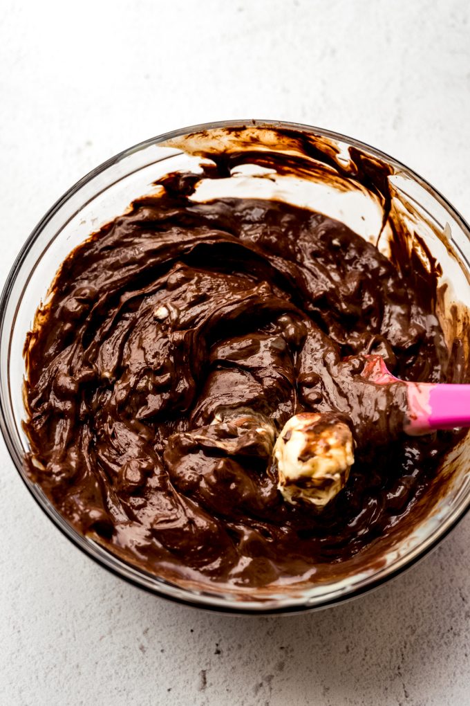 Someone is using a spatula to stir a bowl of chocolate chips and sweetened condensed milk together to make microwave fudge.