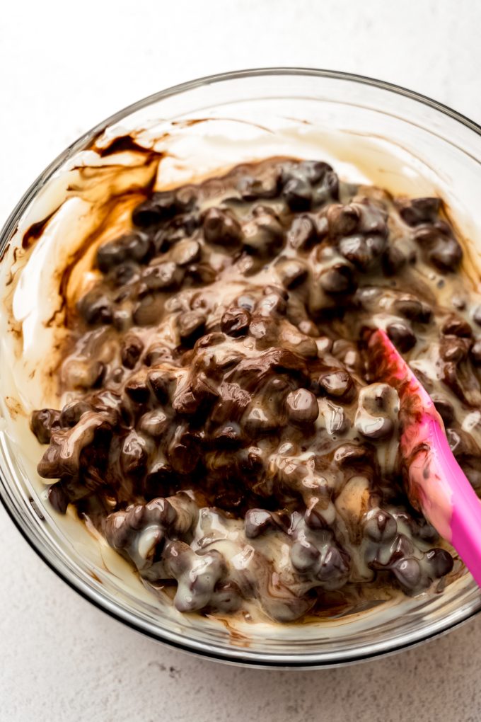 Someone is using a spatula to stir a bowl of chocolate chips and sweetened condensed milk together to make microwave fudge.