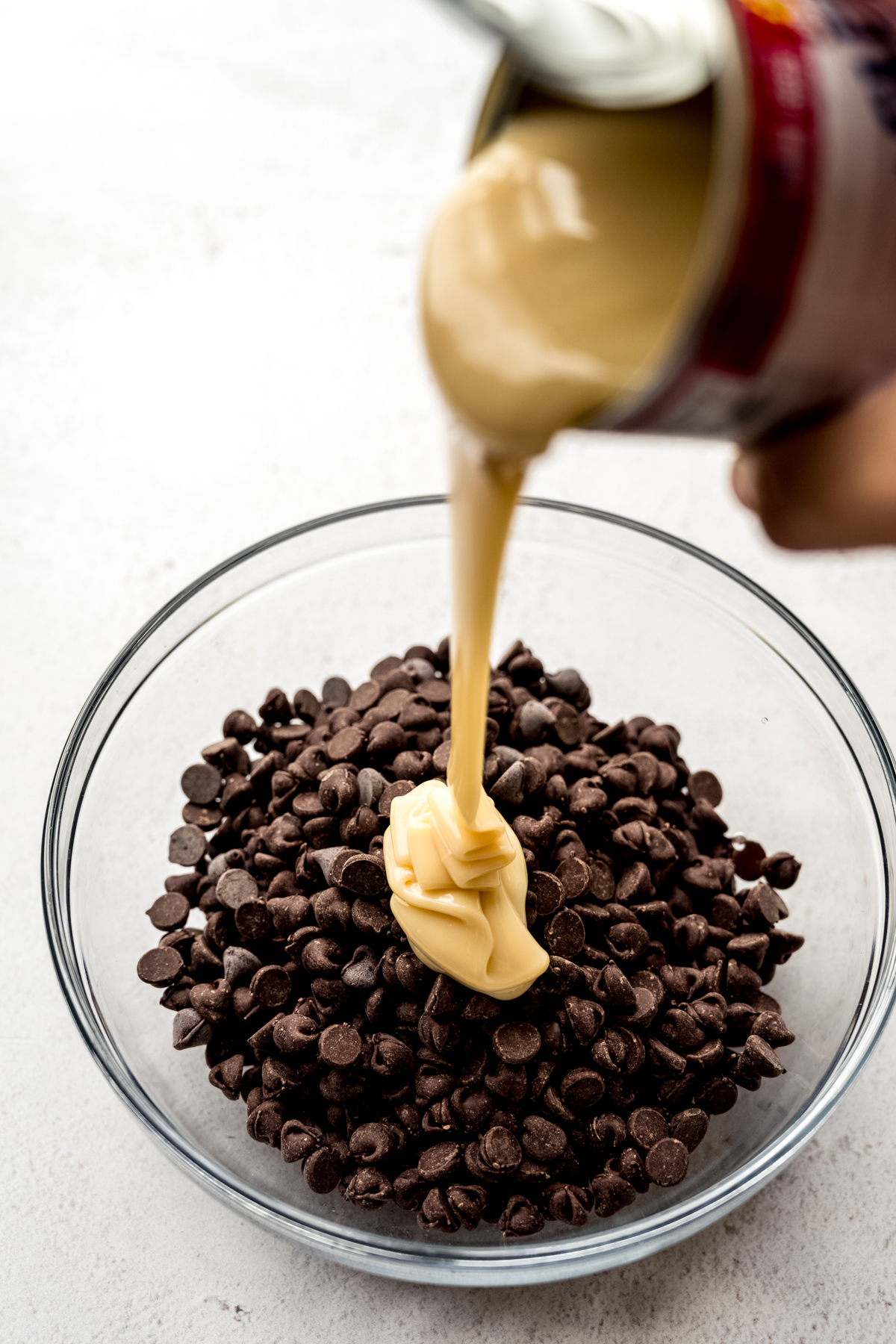 Someone is pouring sweetened condensed milk into a bowl of chocolate chips.