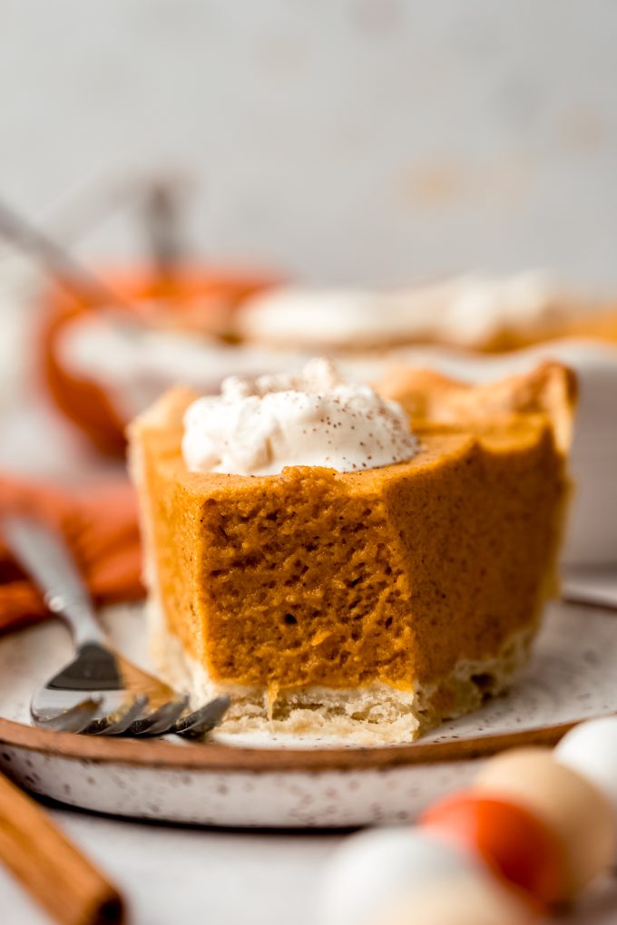 A slice of pumpkin chiffon pie with a bite taken out of it sitting on a plate.