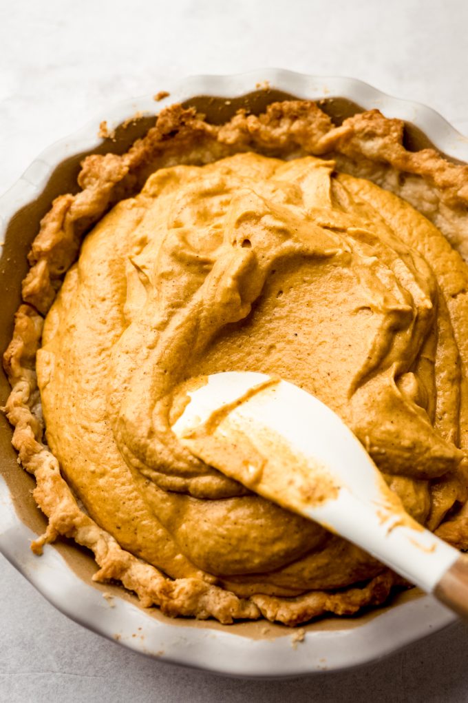 Someone is using a spatula to spread pumpkin chiffon pie filling into a pie crust.
