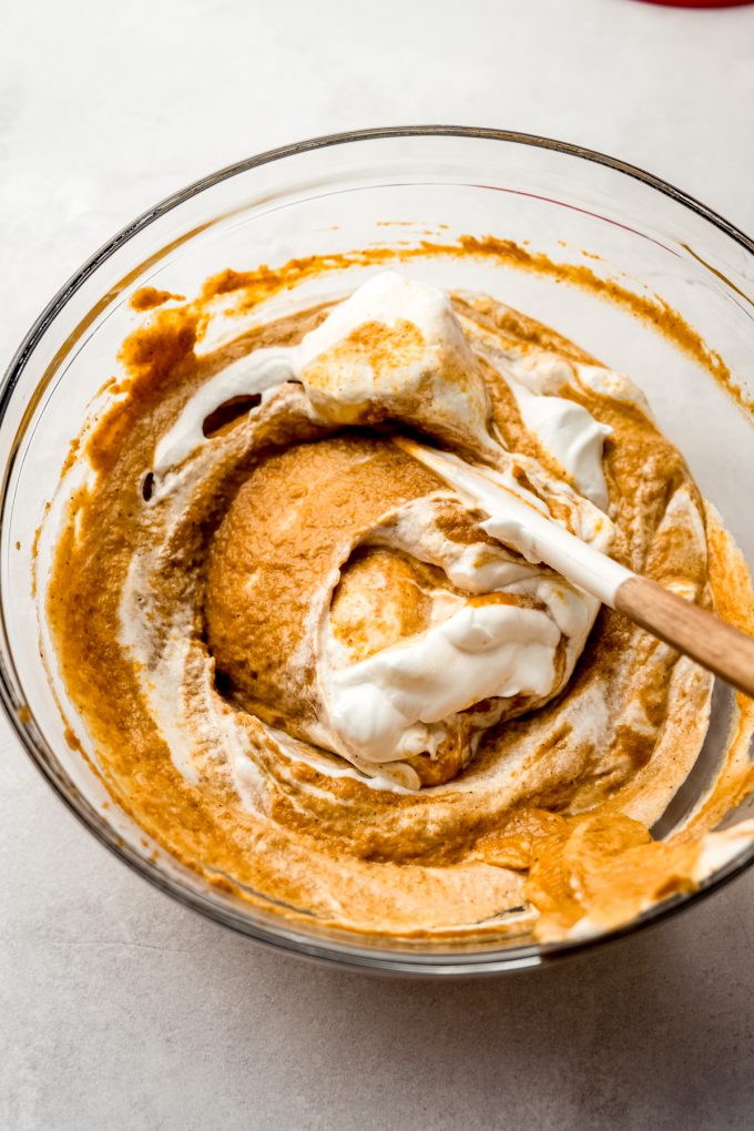 A bowl of the filling for pumpkin chiffon pie getting meringue folded into it with a spatula.
