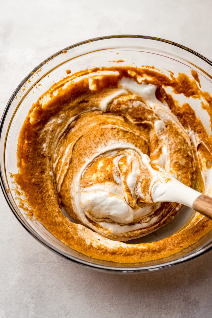 A bowl of the filling for pumpkin chiffon pie getting meringue folded into it with a spatula.