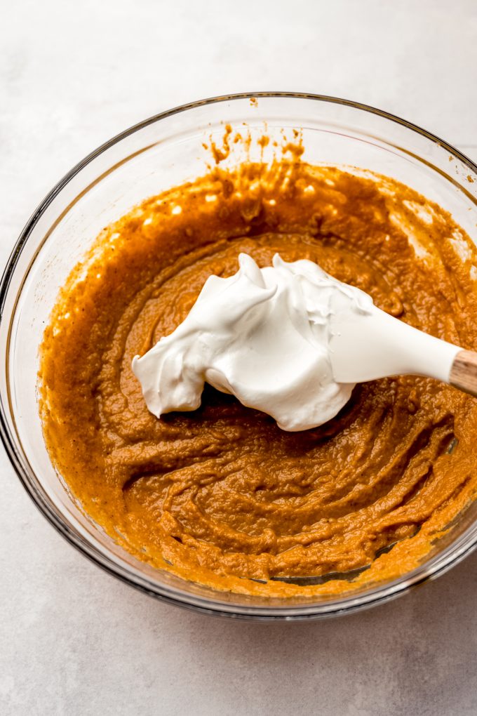 A bowl of the filling for pumpkin chiffon pie getting meringue folded into it with a spatula.