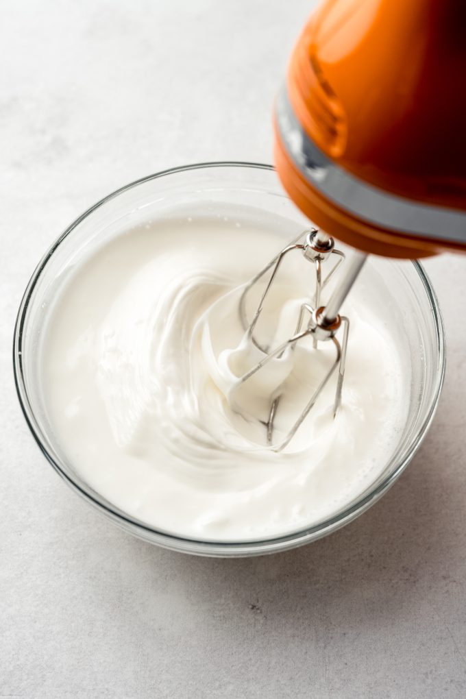 Electric beaters beating egg whites in a small bowl.