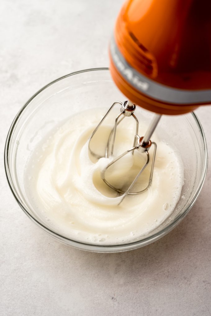 Electric beaters beating egg whites in a small bowl.