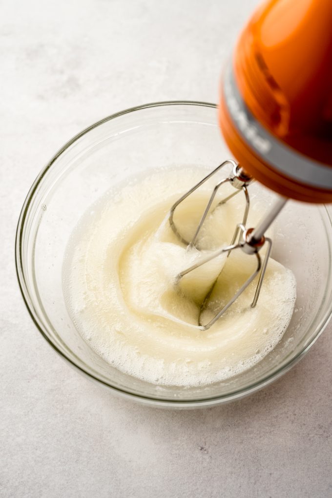 Electric beaters beating egg whites in a small bowl.