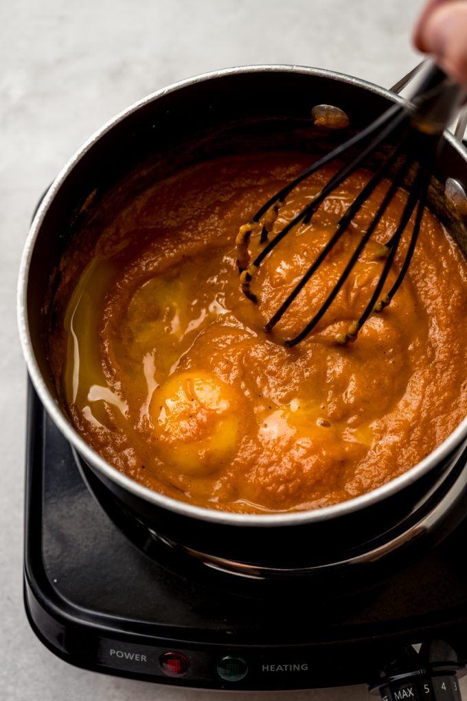 A saucepan of ingredients to make the filling for pumpkin chiffon pie being whisked while heated.