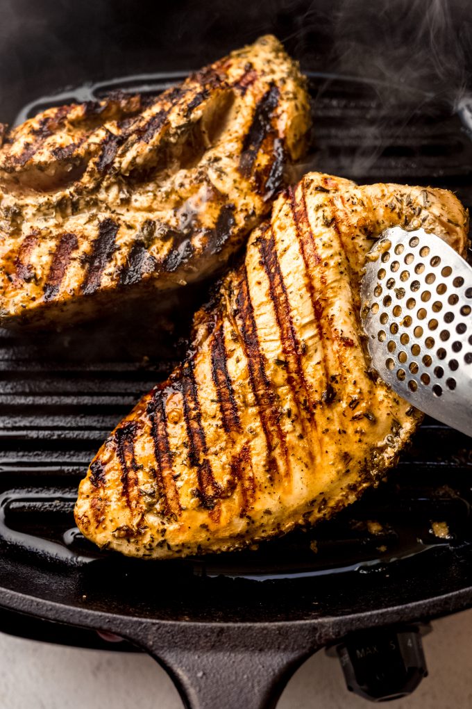 Someone is using tongs to flip a tenderloin of turkey over on a cast iron skillet grill.