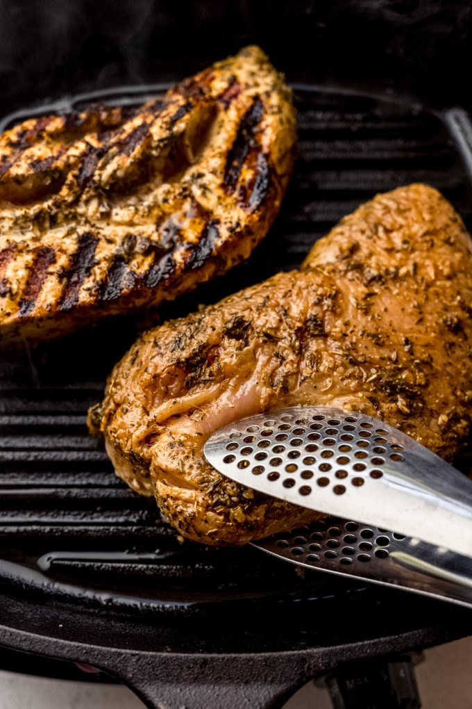 Someone is using tongs to flip a tenderloin of turkey over on a cast iron skillet grill.