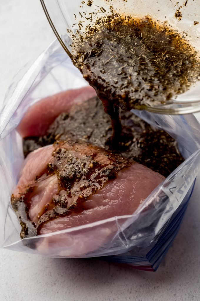 Someone is pouring marinade into a zip top bag with turkey tenderloin in it.