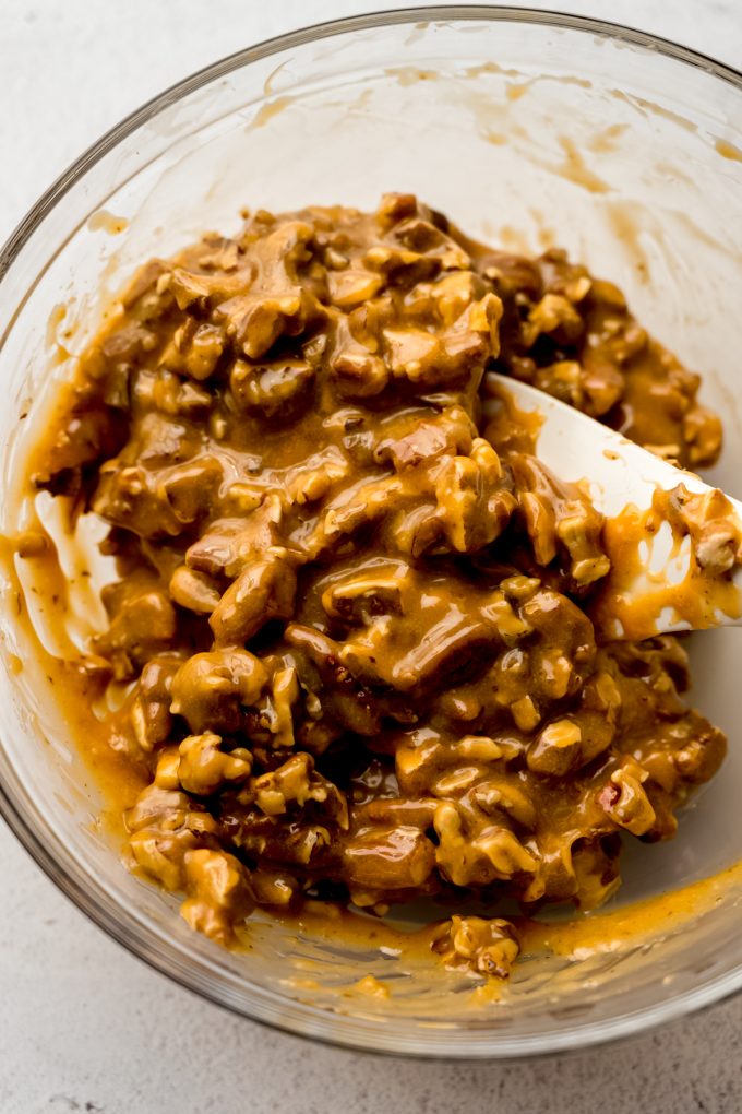 Someone is stirring caramel and pecans together to make homemade turtles.