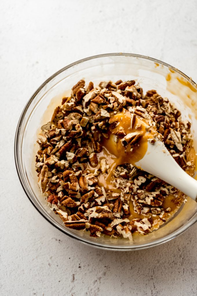 Someone is stirring caramel and pecans together to make homemade turtles.