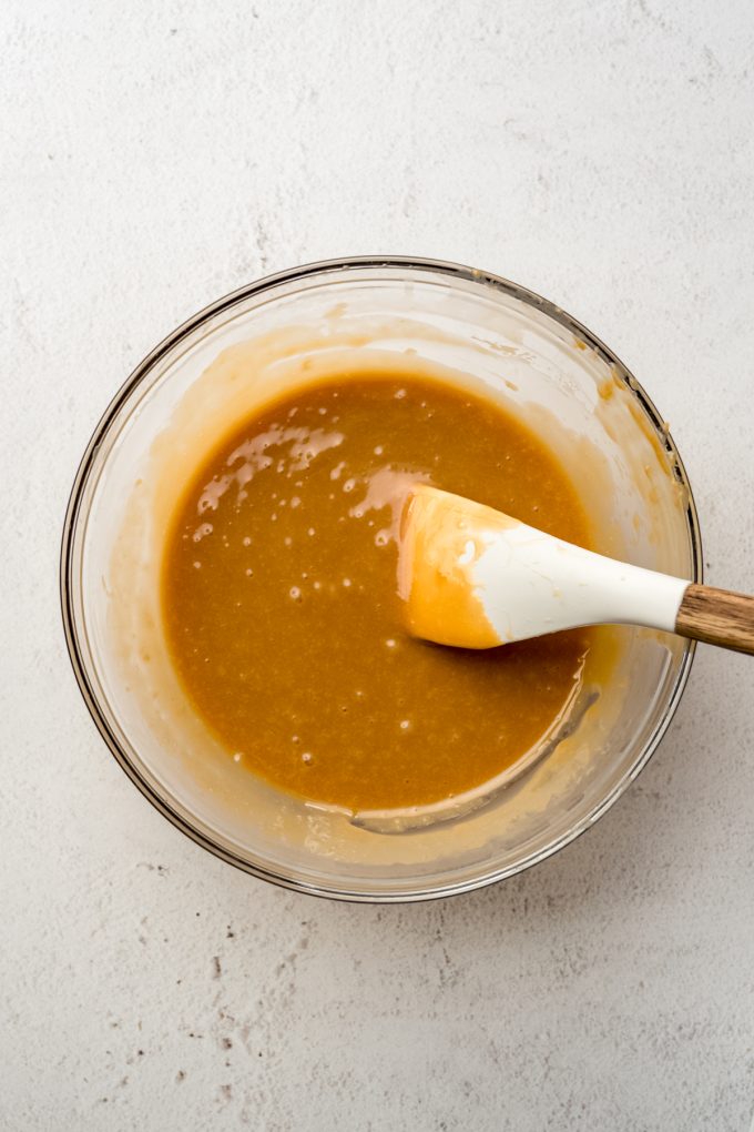 A bowl of caramel and heavy cream melted with a spatula in it.