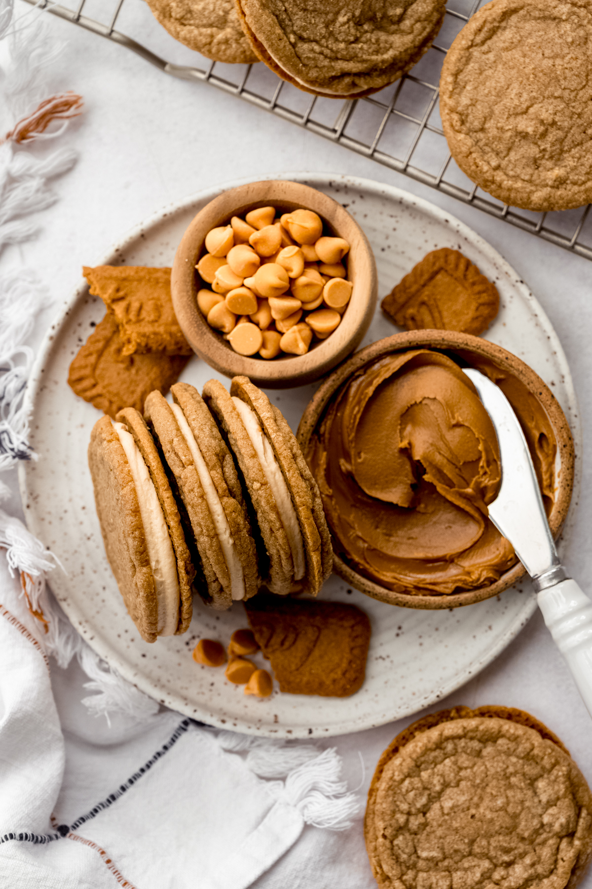 A plate of Biscoff sandwich cookies with a small bowl of butterscotch chips and a bowl of Biscoff spread on it.