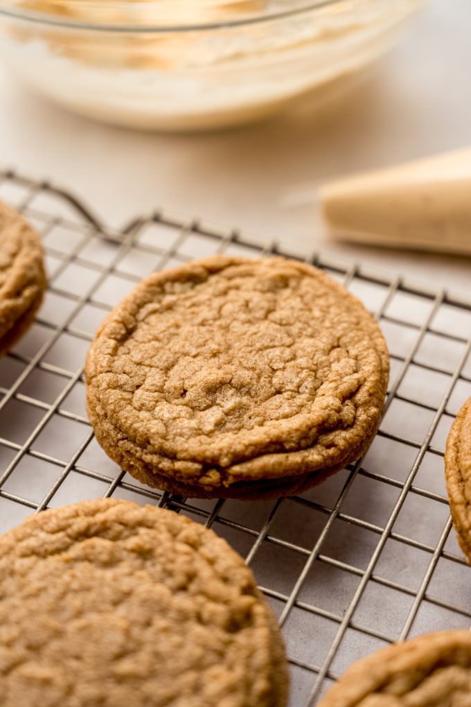 A cooling rack with Biscoff cookies on it and a piping bag of butterscotch marshmallow frosting in the background.