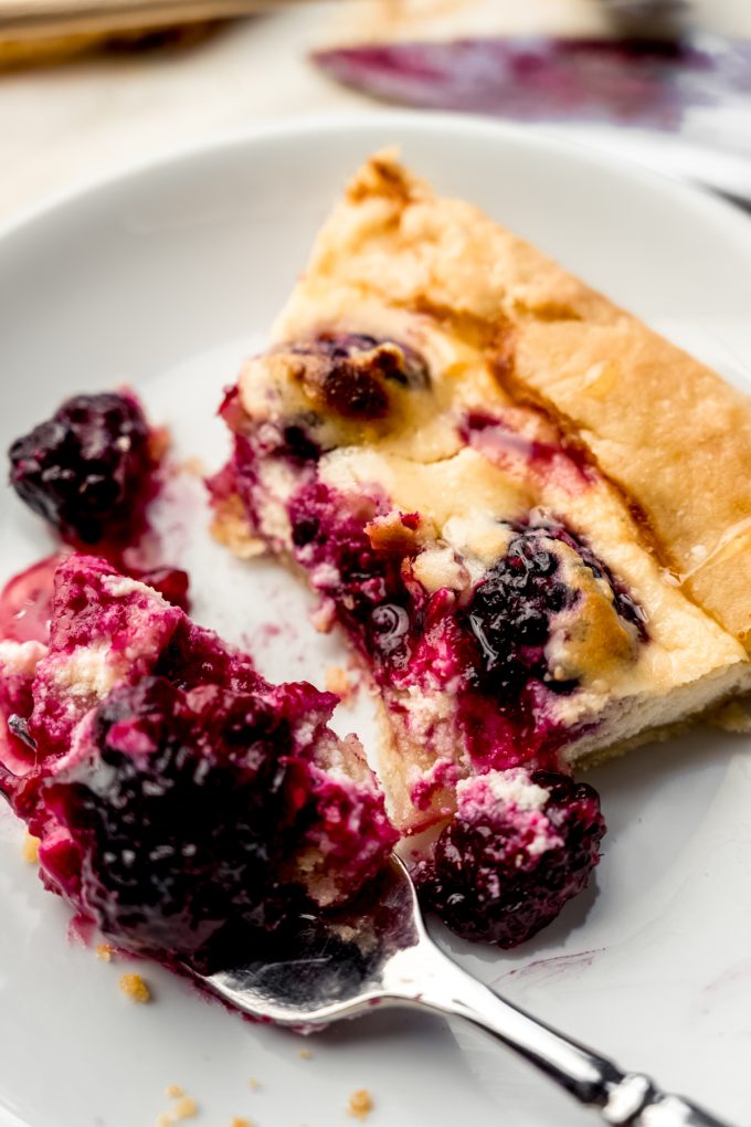A slice of blackberry galette on a plate with a fork that has a bite on it.
