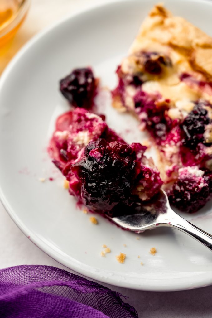 A slice of blackberry galette on a plate with a fork that has a bite on it.