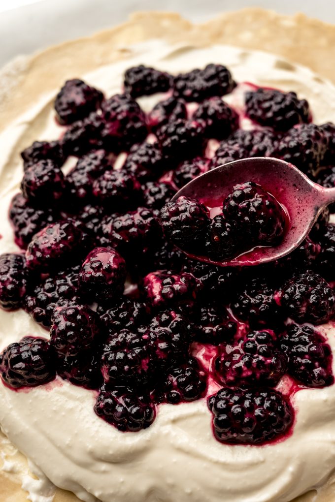 Someone is spooning blackberries onto the whipped feta later of a blackberry galette.