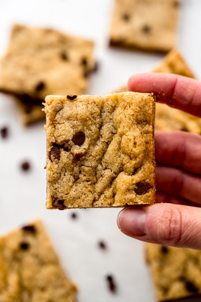 Someone is holding a center piece of a batch of chocolate chip cookie bars.