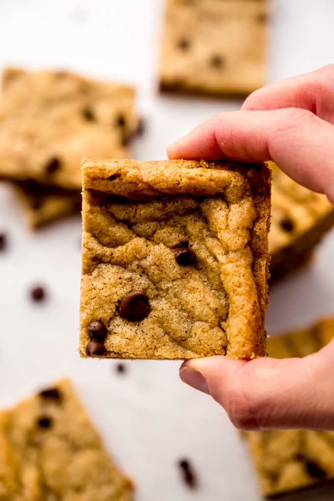 Someone is holding an edge piece of a batch of chocolate chip cookie bars.