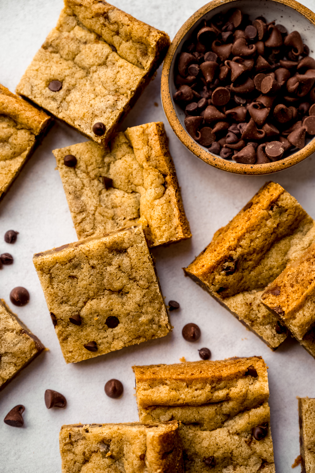 Aerial photo of sliced chocolate chip cookie bars on a surface with a bowl of chocolate chips.
