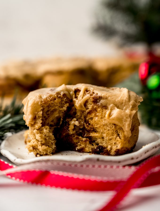 A gingerbread cinnamon roll on a plate with a bite taken out of it.