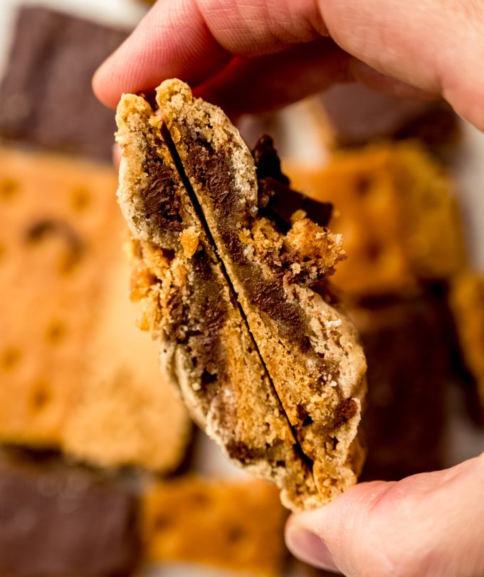 Someone is holding a graham cracker toffee cookie that has been cut in half so you can see the cross section.