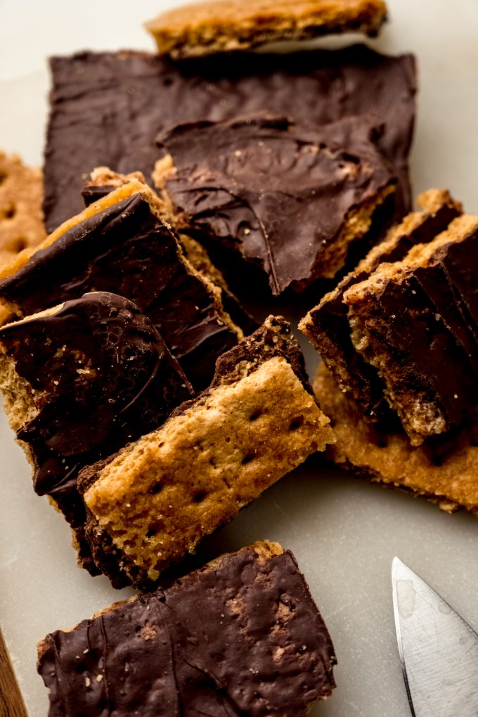 Pieces of graham cracker toffee on a cutting board with a knife.
