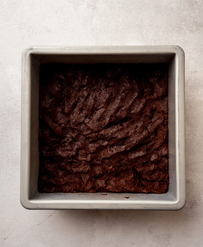 Chocolate chunk cookie dough pressed into a square baking pan.