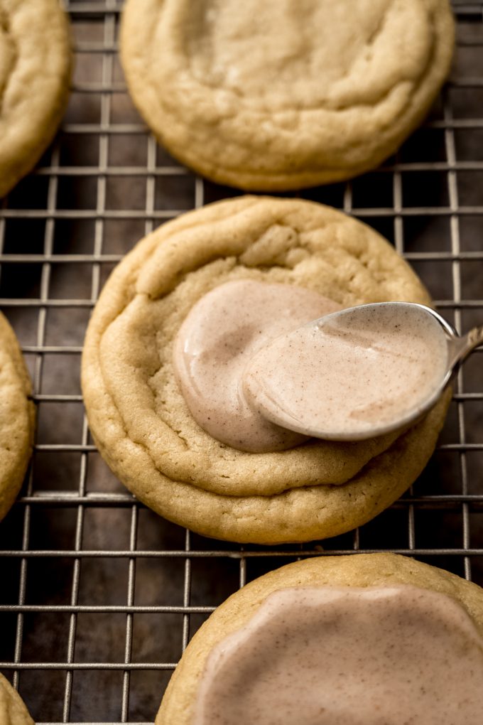 Someone is using a spoon to put icing on a brown sugar Pop Tart cookie that's on a cooling rack.