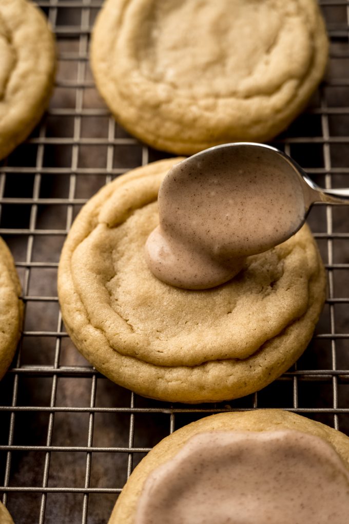 Someone is using a spoon to put icing on a brown sugar Pop Tart cookie that's on a cooling rack.