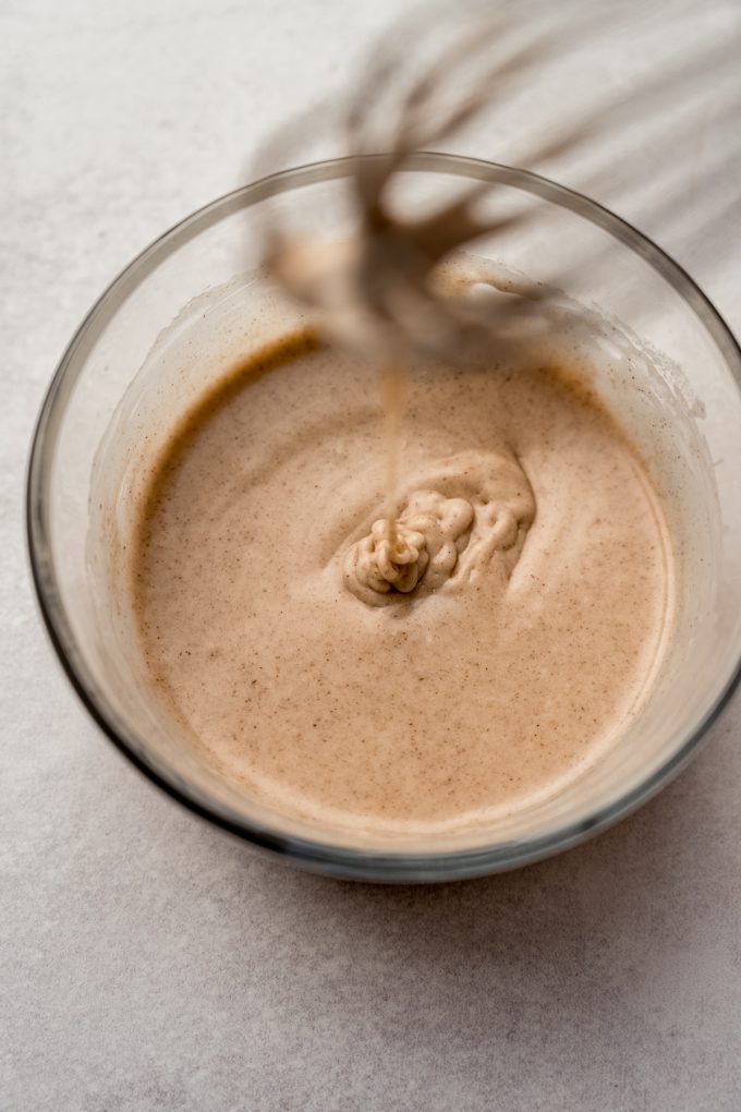 A bowl of cinnamon sugar glaze for cookies with a whisk in it.