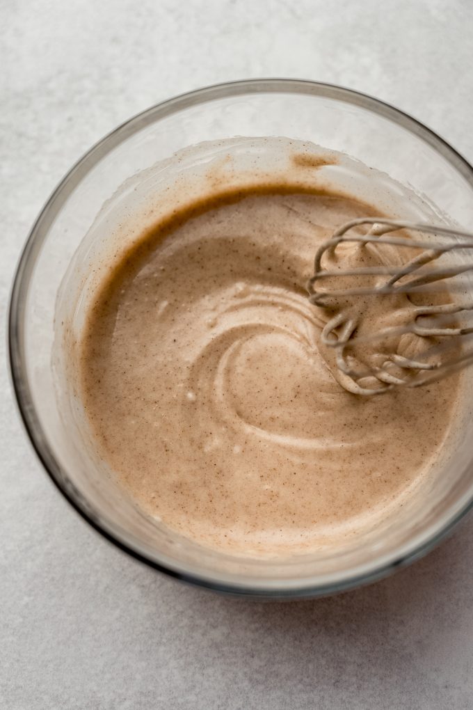 A bowl of cinnamon sugar glaze for cookies with a whisk in it.