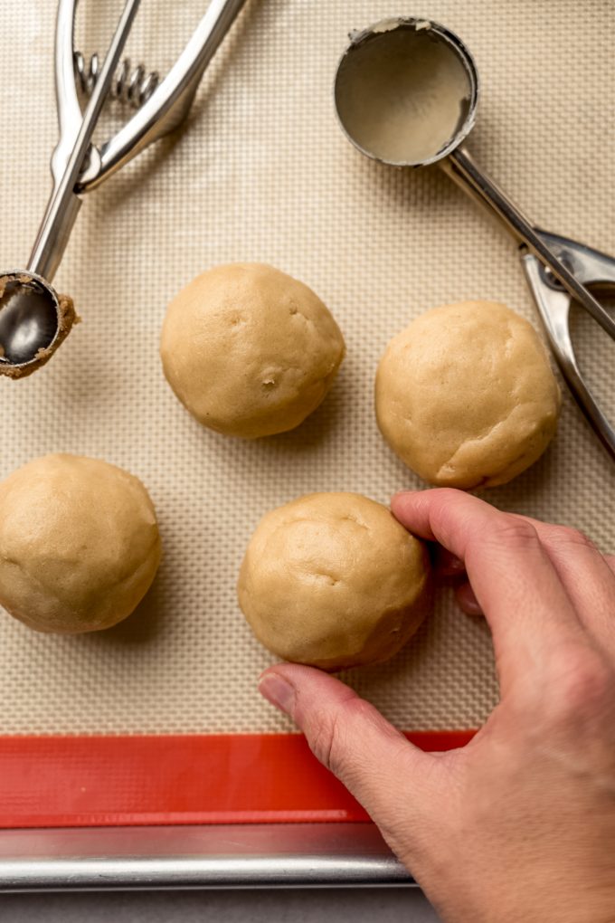 Aerial photo of Pop Tart cookie dough balls on a baking sheet and someone is holding one to show size.