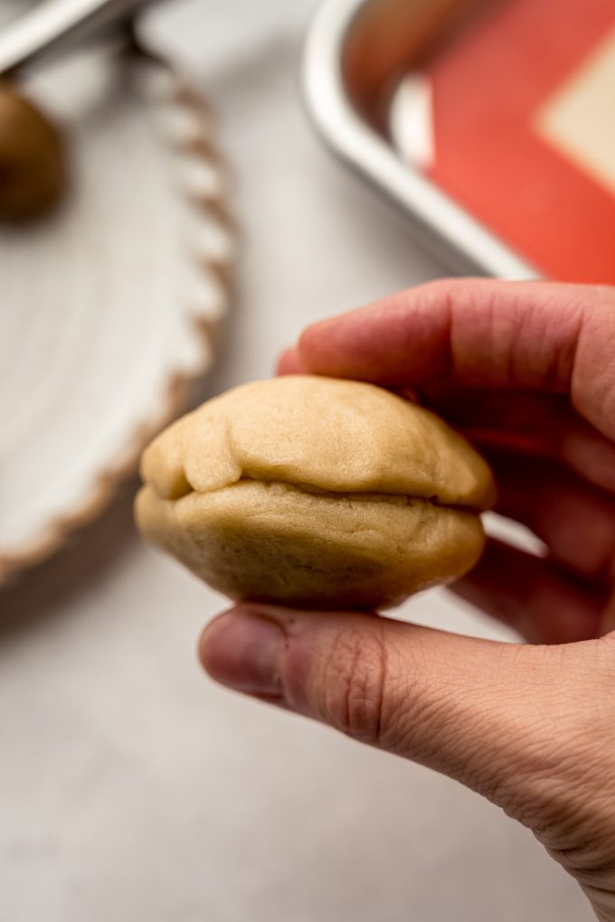 Someone is holding a cookie dough ball that has been stuffed with brown sugar filing.