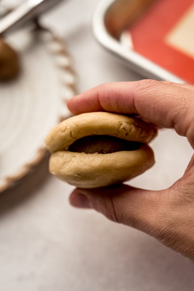 Someone is holding a cookie dough ball that has been stuffed with brown sugar filing.