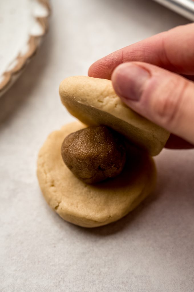 Someone is making a cookie dough ball sandwich with brown sugar filling inside.