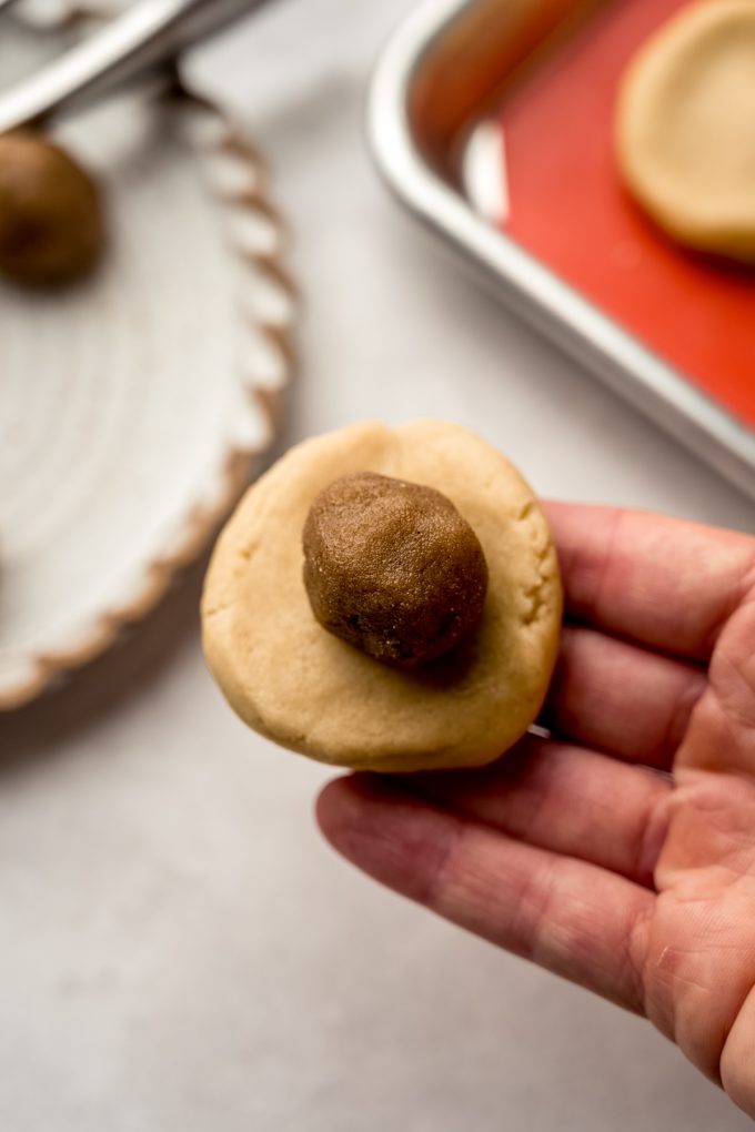 Someone is holding a disc of cookie dough with a ball of brown sugar filling in it to make a stuffed cookie.