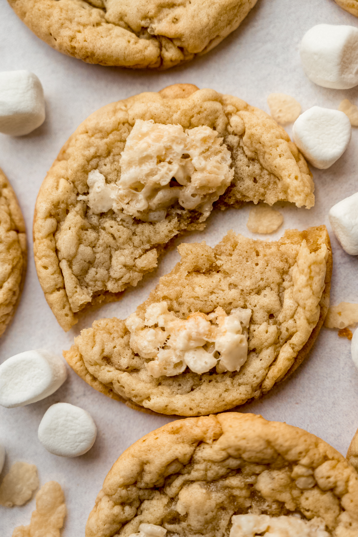 Rice Krispie cookies on a surface with mini marshmallows and cereal around it.
