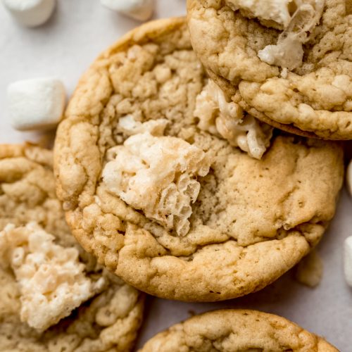 Rice Krispie cookies on a surface with mini marshmallows and cereal around it.