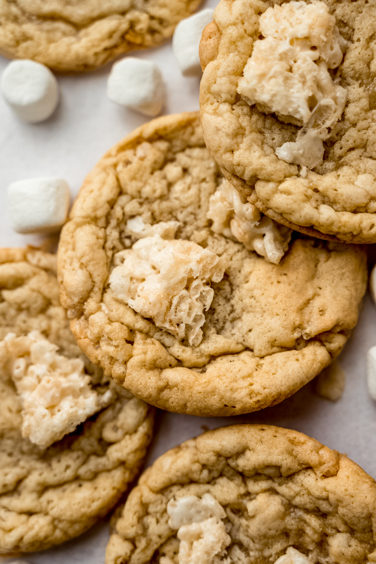 Rice Krispie cookies on a surface with mini marshmallows and cereal around it.